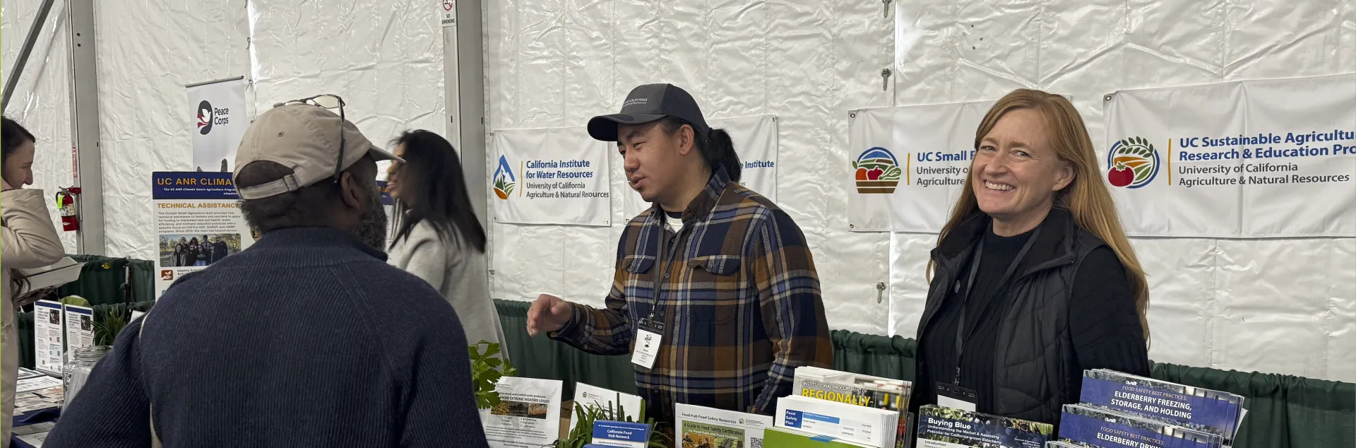 Two UC ANR representatives speak with an attendee during the EcoFarm 2026 conference.