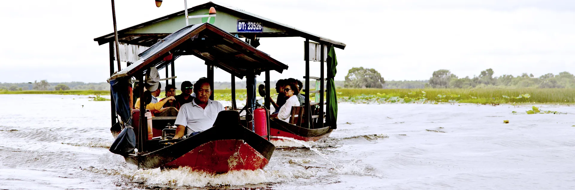 Man drives a boat pulling another boat containing passengers across the water