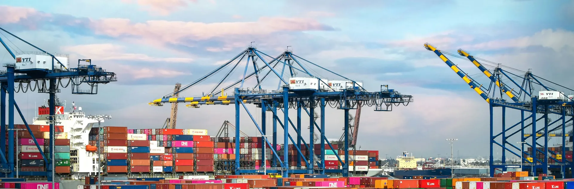 The Port of Los Angeles filled with brightly colored shipping containers and a container ship docked next to cranes.