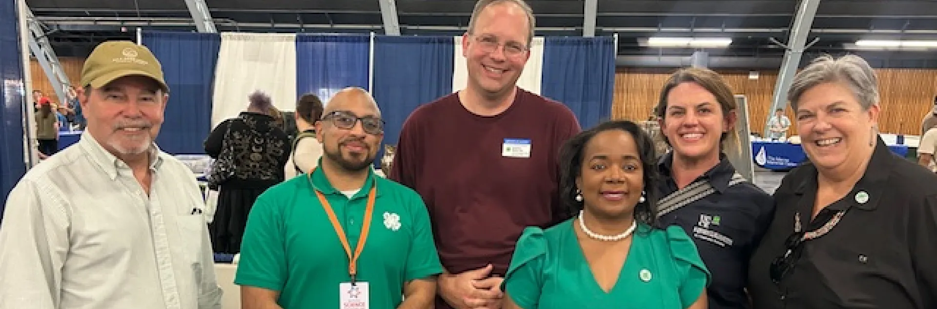 Six people stand in a row. A man and a woman are wearing 4-H green