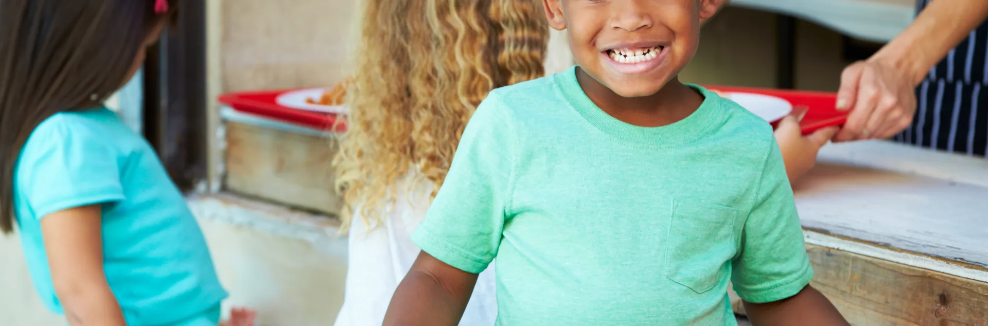A young boy holds a red tray with a plate of fresh, school food while standing in line at the school cafeteria.