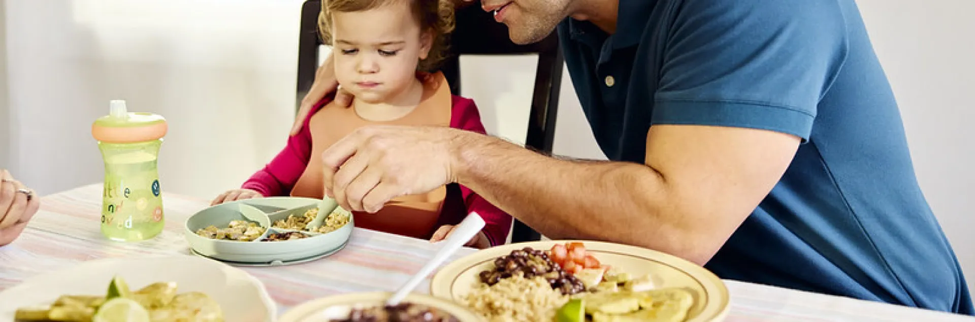 A father helps his infant eat dinner.