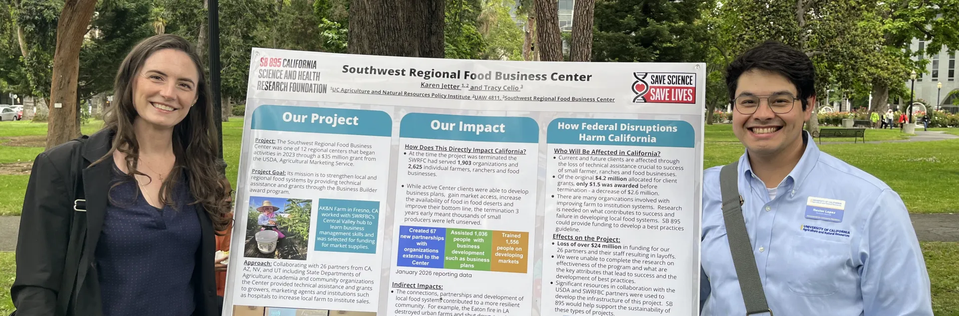 Anne and Nestor stand on opposite sides of a Southwest Regional Food Business Center poster describing the project, its impact and how federal disruptions harm California.