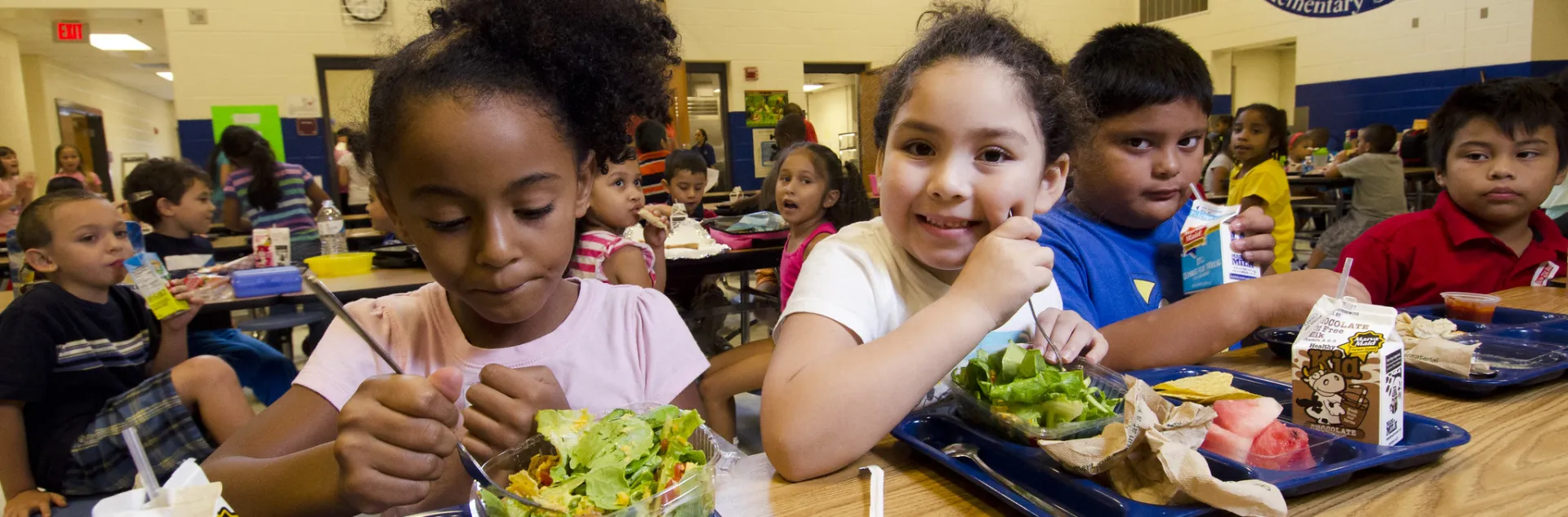 A group of elementary school children eat lunch in their school cafeteria off reusable trays.