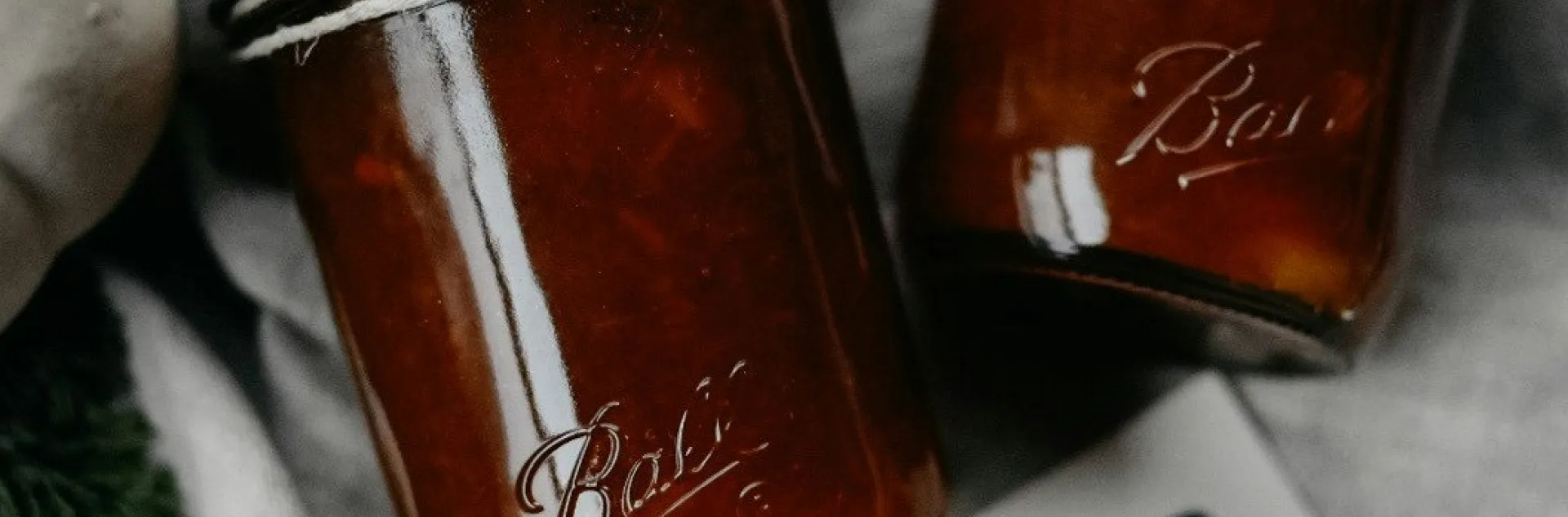 two ball mason jars containing carrot cake jam tied with twine sitting on top of a printed recipe page