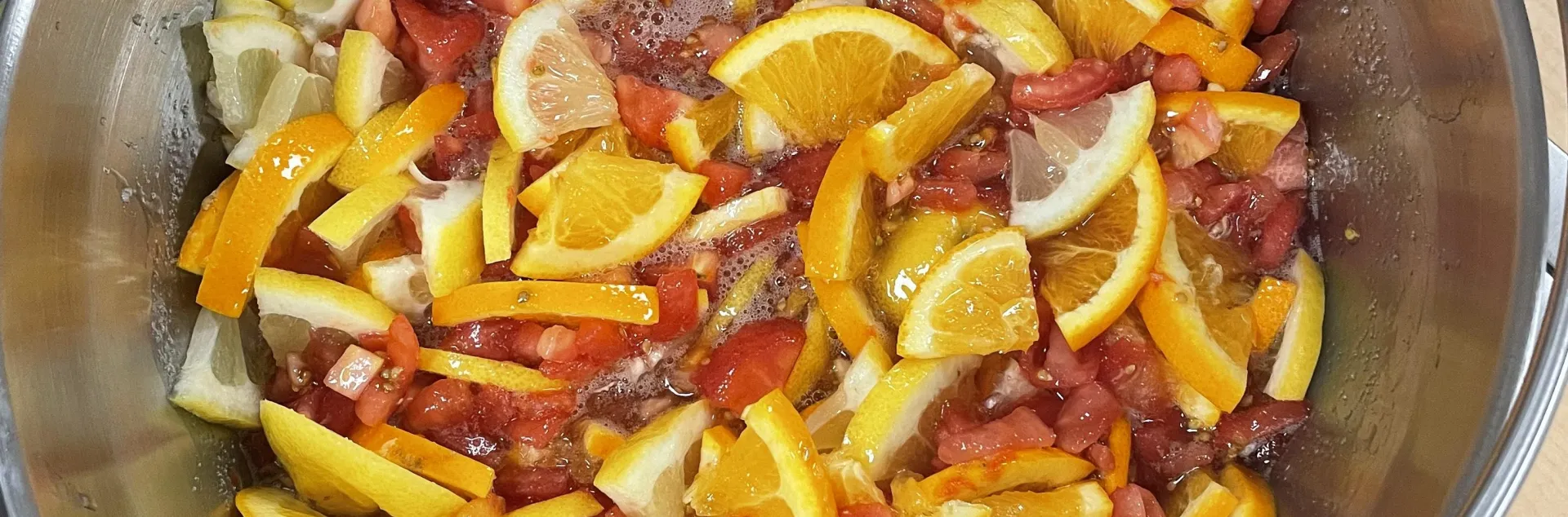 a pot of ingredients used to make tomato marmalade including cut tomotoes and citrus