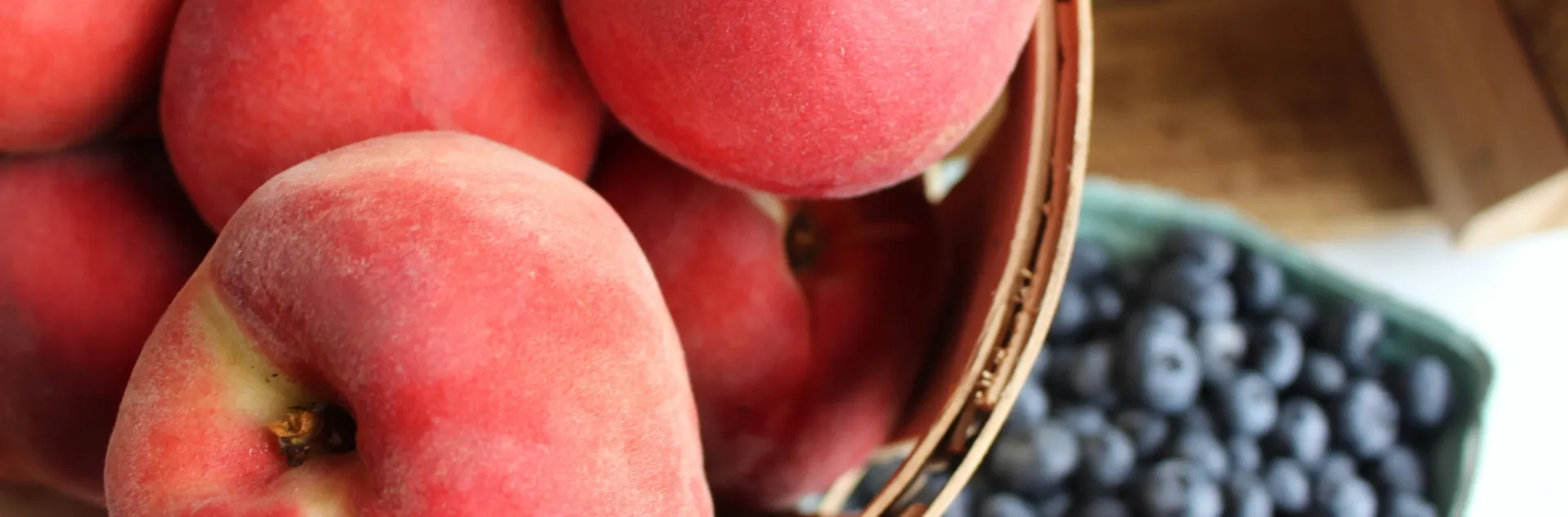 a bowl of several pink peaches next to a bowl of blueberries
