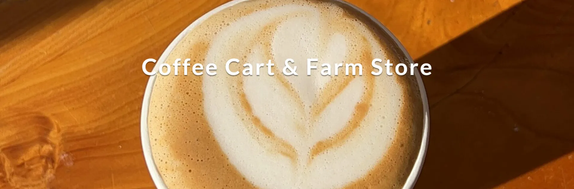 A close-up overhead view of a coffee drink with plant-shaped foam art. Its cup sits on a wooden surface. Text overlay reads "Coffee Cart & Farm Store."