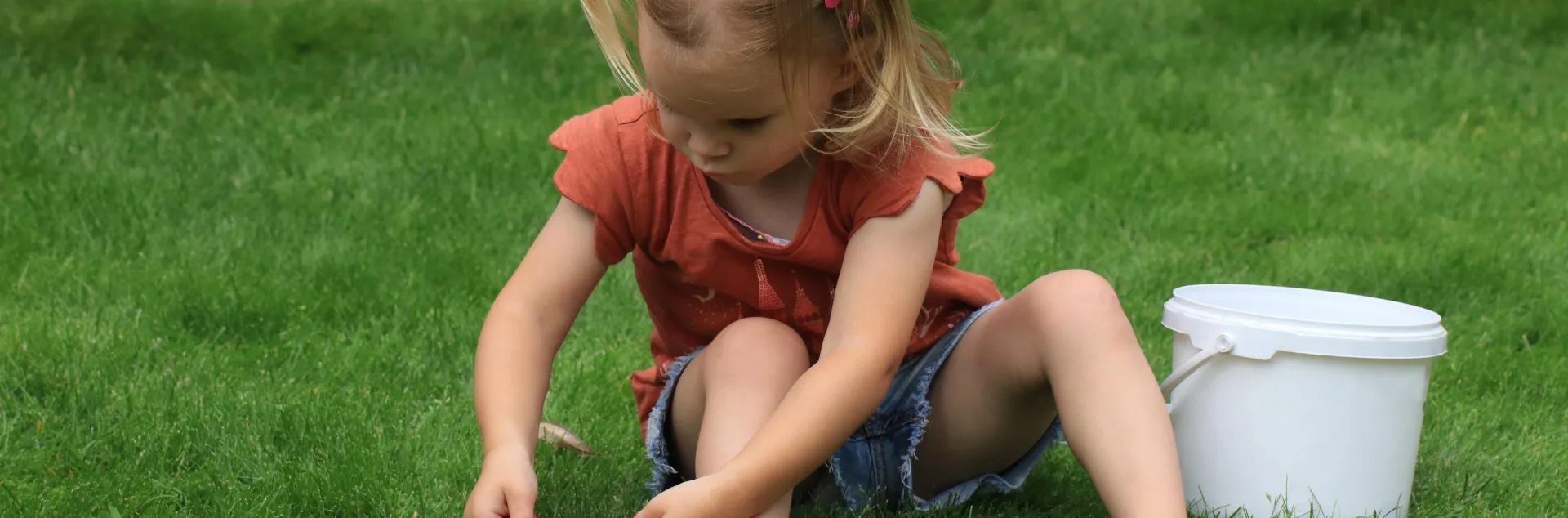 Photo of young child sitting on grass, cutting it with children's scissors. (Marjon Besteman on Pixabay)