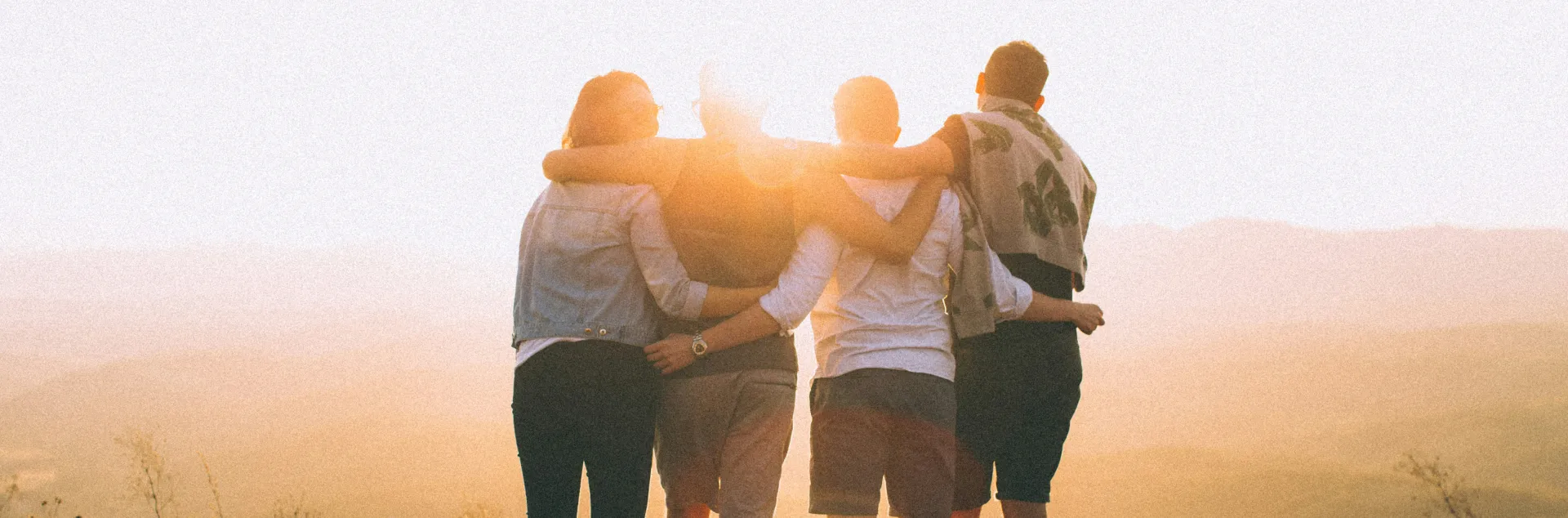 Group of people with arms around each other, watching the sunset