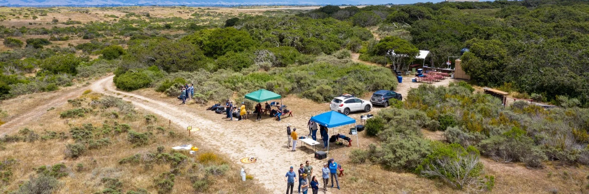 An aerial view of people standing under a tent in scrubland