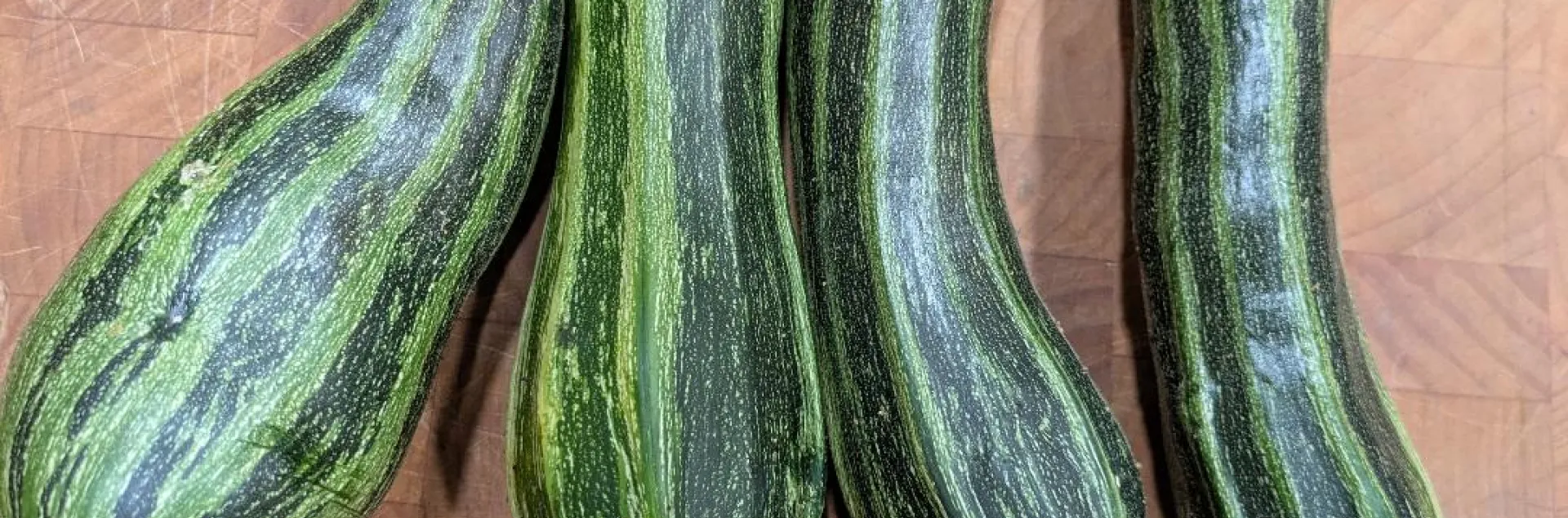 Four Italian striped zucchini on a wooden cutting board.
