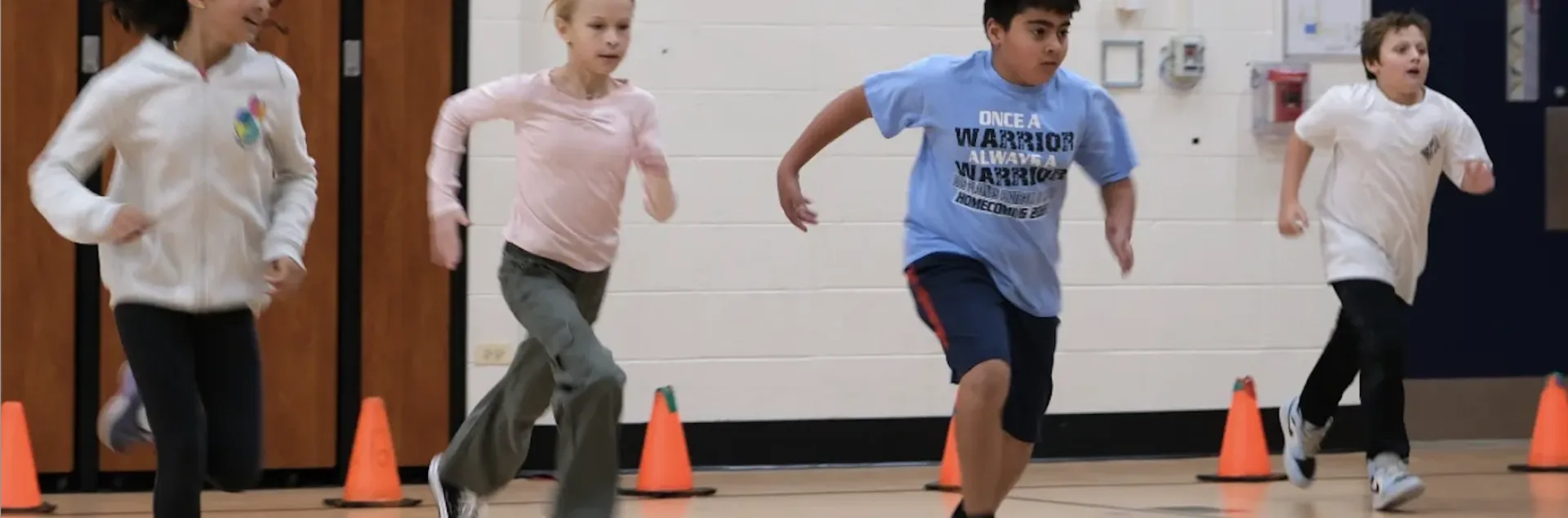 Image of four adolescents performing a school-based physical fitness test indoors.