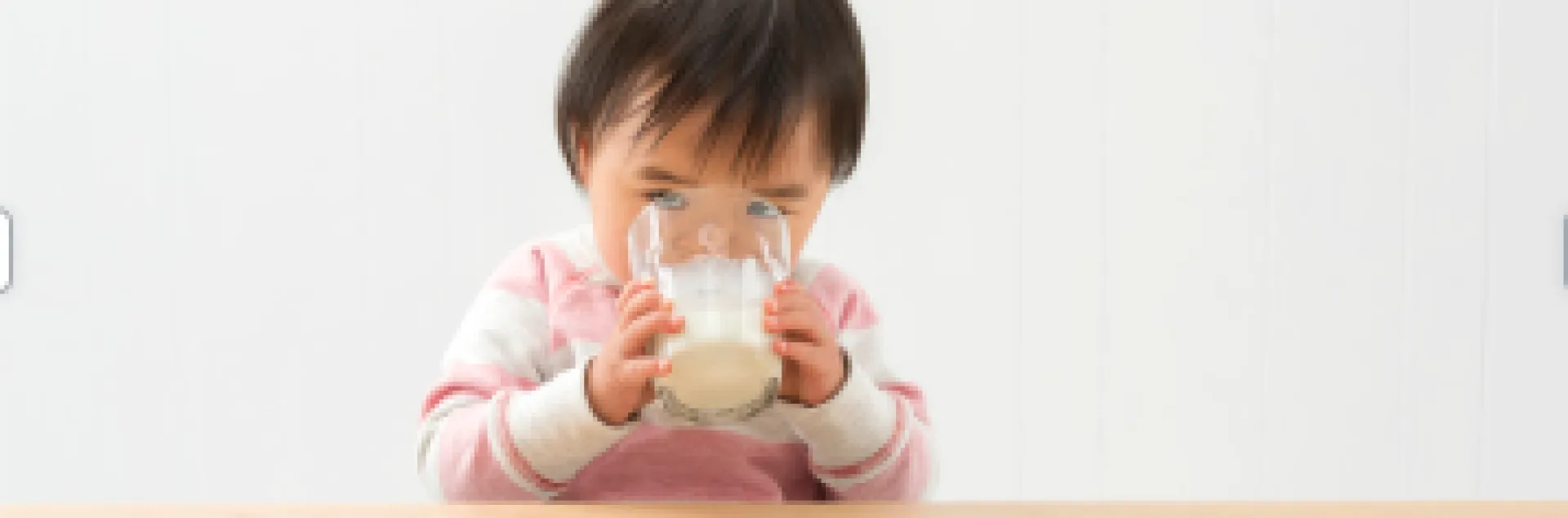Small child wearing pink outfit holding glass with two hands drinking milk