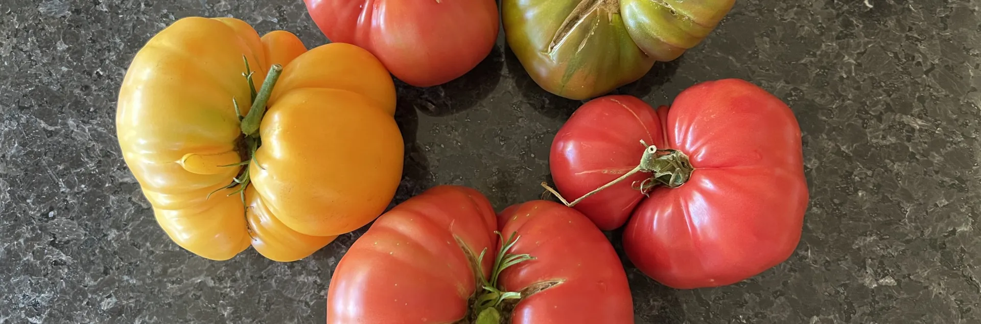 Red, yellow, and green heirloom tomatoes on a dark, marbled counter.