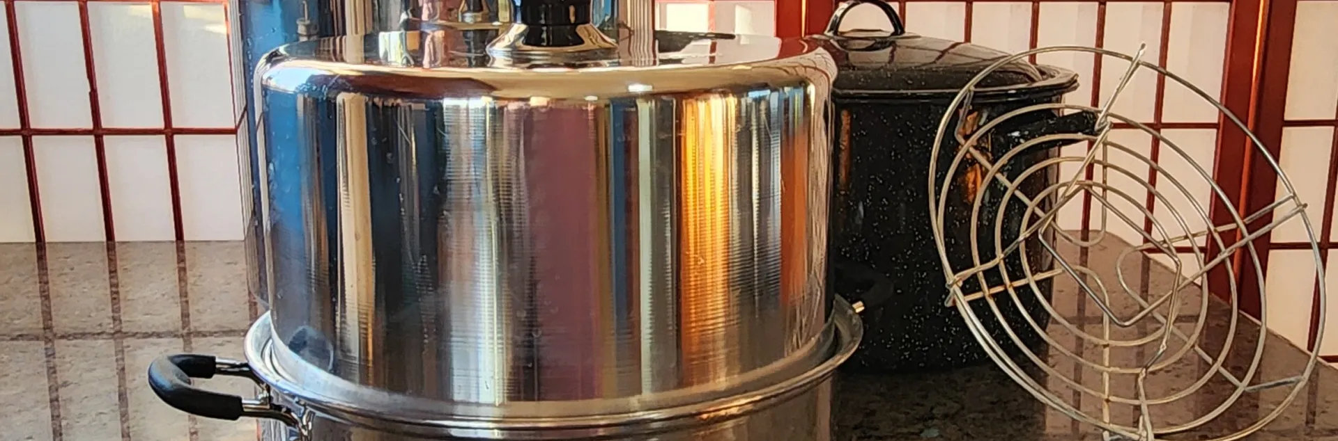 Pressure, steam, and water bath canners with a rack on a dark, granite counter.