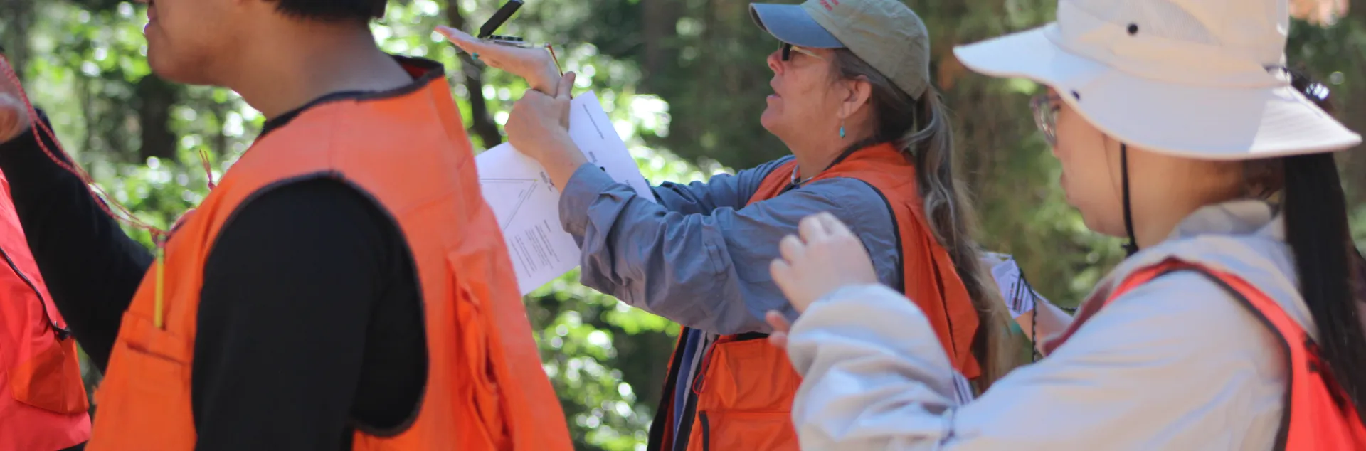 Group of people in orange vests use a compass.