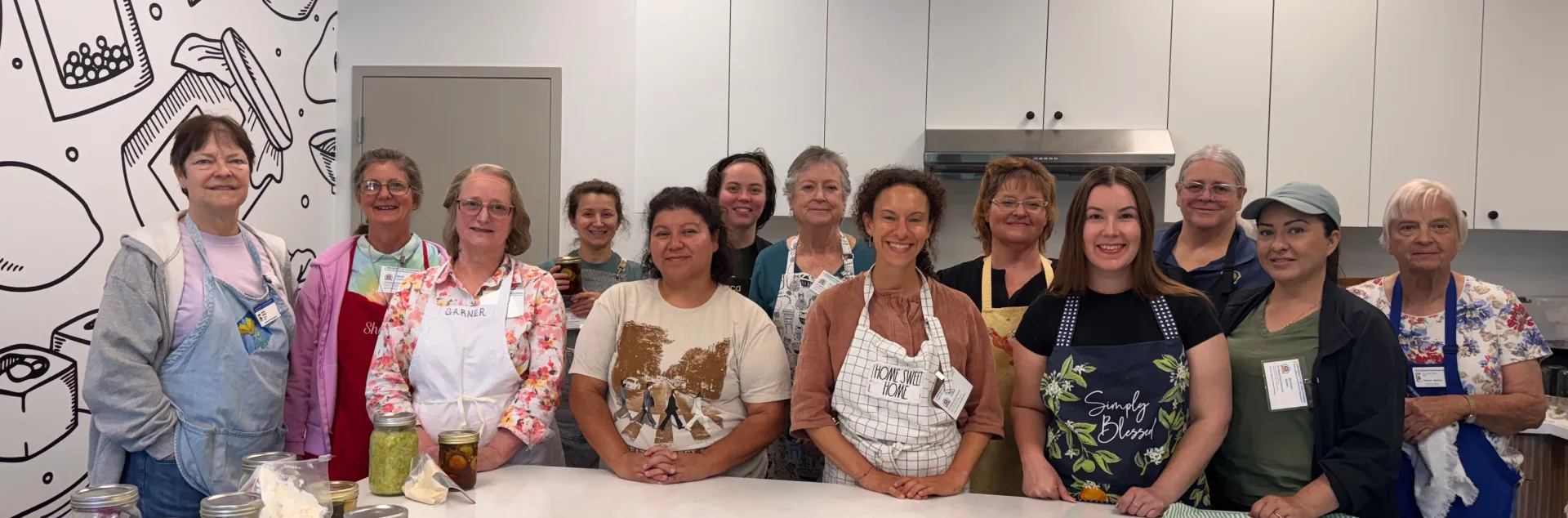 Group of volunteers in training smiling in a kitchen behind a row of canned foods