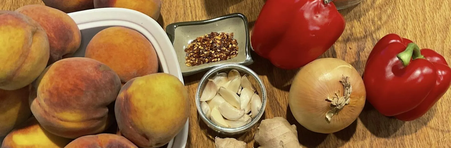 Peaches, garlic, peppers, onions, and ginger on a wood surface.