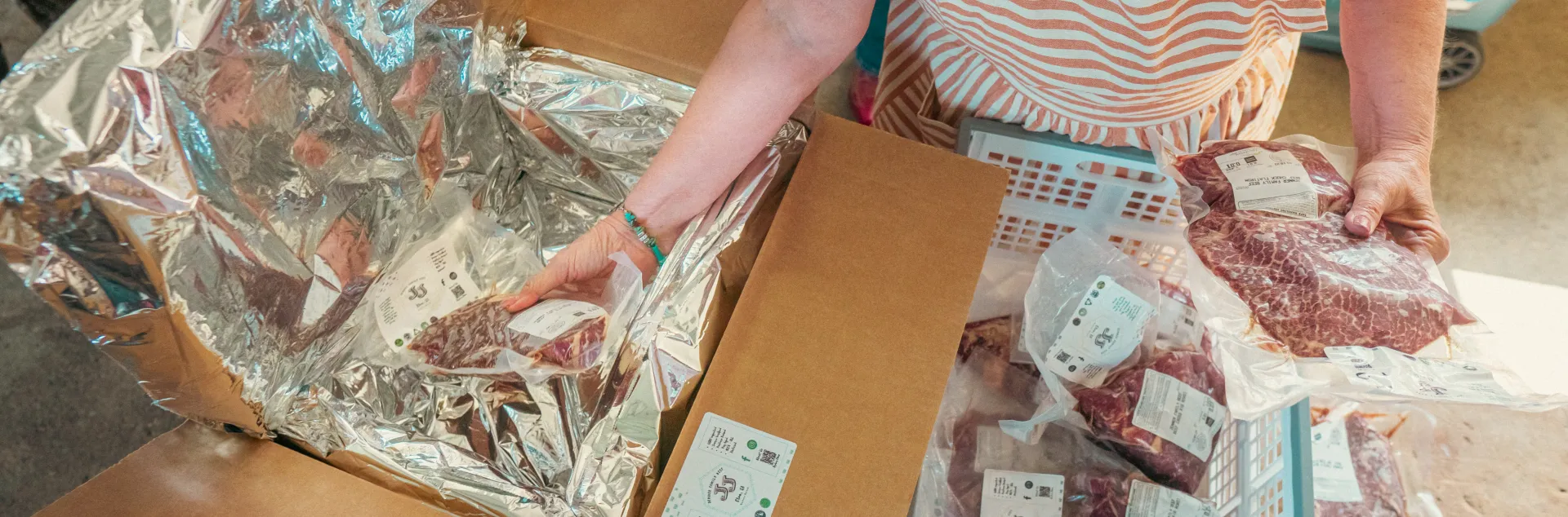A person wearing an apron places vacuum-packed beef into a lined cardboard shipping box.