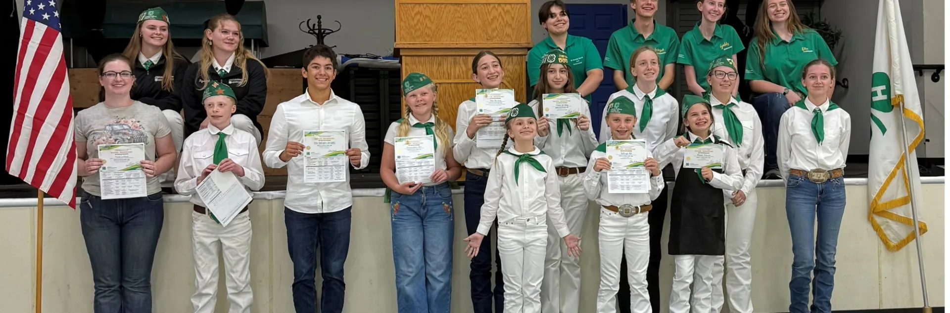 4-H members stand in front of a stage with their public speaking contest awards.