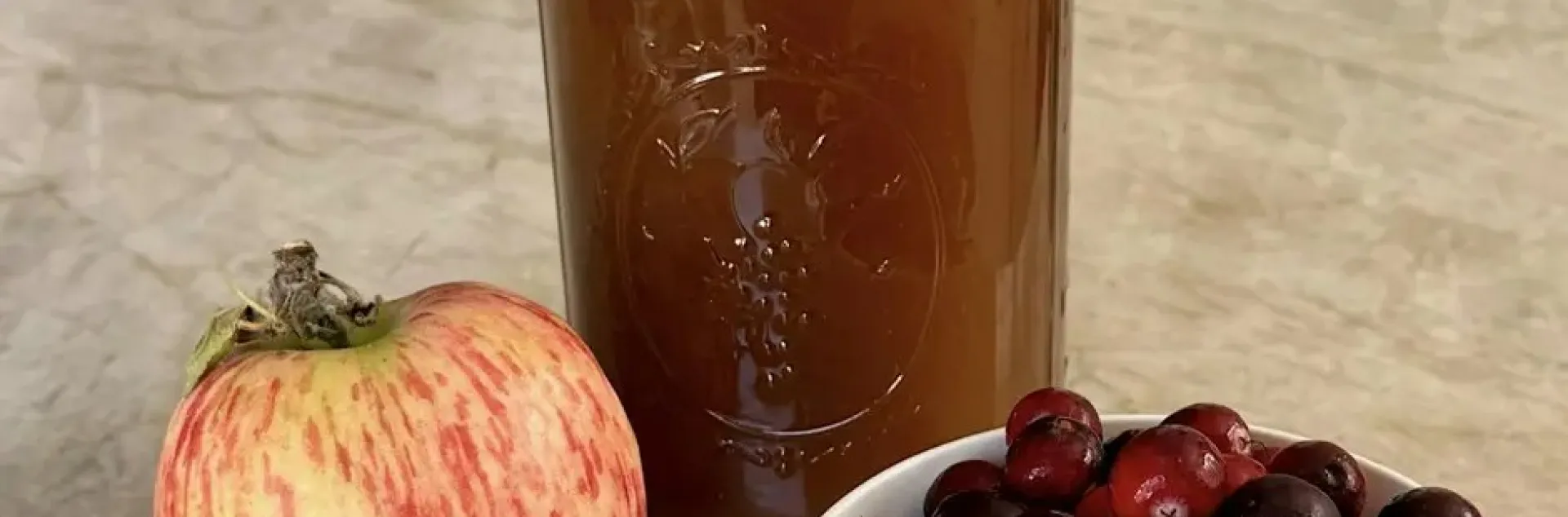 An apple and bowl of cranberries next to a jar of juice.