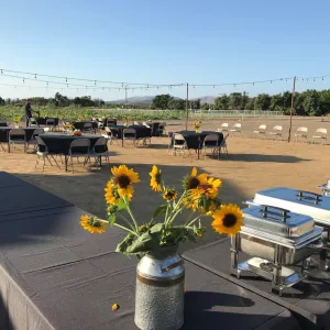 outdoor annex area set up with round tables and chairs, and buffet style food set up, with string lights and flowers for an event