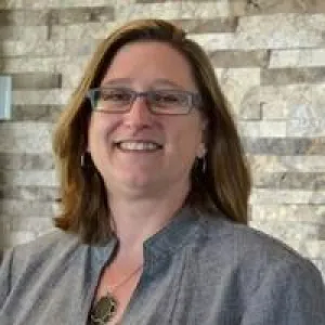 Woman with glasses and gray jacket, with a gray background