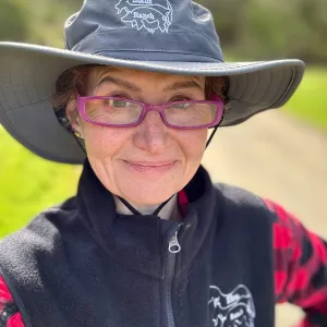 Monique is standing outside in the sunlight wearing glasses and an Elkus branded hat and vest