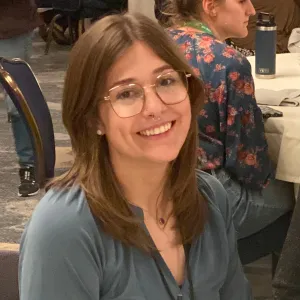 white woman with medium brown hair in a blue shirt and glasses smiling