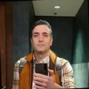 a man taking a mirror selfie wearing a flannel and vest
