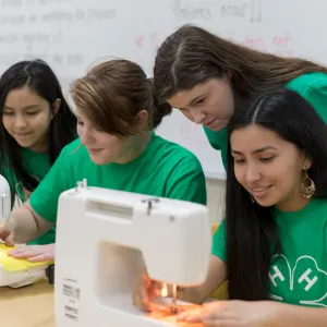 4-H members in Green shirts gathered around a sewing machine
