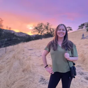 Person standing in a field with sunset and oak trees in background
