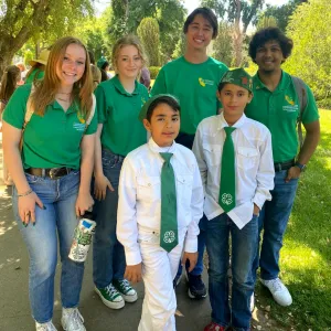 A group of youth in 4-H apparel. The back row wears green 4-H Polos the two kids in front all white with green 4-H ties. 