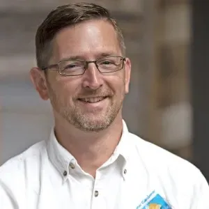 man with light brown hair and glasses wearing a white shirt with the UC Master Gardener logo