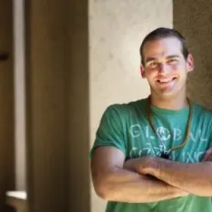 man wearing a green shirt with his arms crossed leaning against a pillar