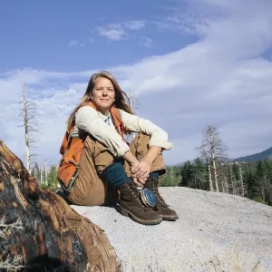A photo of Forest Advisor, Susie Kocher. She is sitting on a rock in a forest.