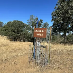 Labeled emergency water source outdoor on a property. The exposed water source pipe has a fence around it and has an identifying sign hung on the fence.