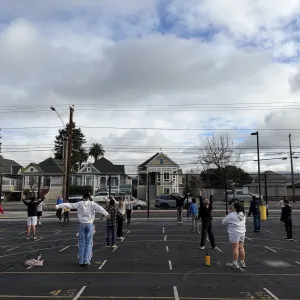 Elementary school students play outside on the school blacktop with their PE teacher during a cloudy day.
