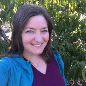 A smiling Master Gardener in a blue and purple shirt with fruit tree leaves in the background.