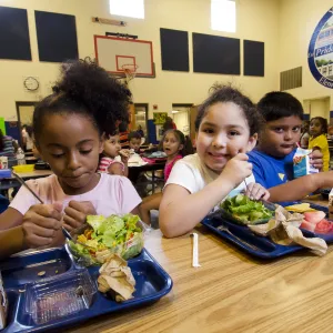 A group of elementary school children eat lunch in their school cafeteria off reusable trays.