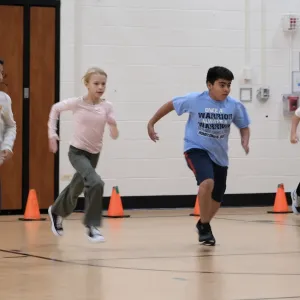 Image of four adolescents performing a school-based physical fitness test indoors. 