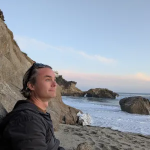A man sitting on a beach looking out over the ocean at sunset.