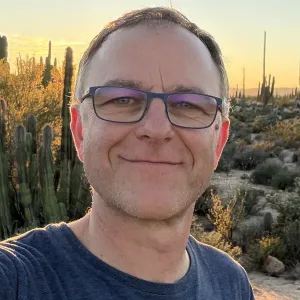 Portrait photo of a person with glasses in sunset light with desert landscape and cactuses in the background.