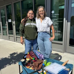 4-H educator Jazmin Vargas stands with 4-H Youth Development Advisor Dr. Sally Neas with a wagon full of cooking supplies outside of San Mateo County's juvenile hall