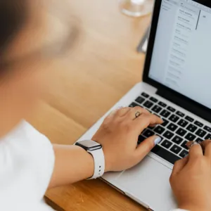 A woman with blue fingernail polish types on a laptop.