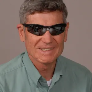 A man smiling, wearing a blue shirt and sunglasses.