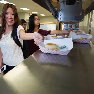 High school students grab paper food boats containing white biscuits and a plastic-packaged jelly condiment for breakfast from their school cafeteria.