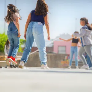 A group of girls play jump rope outside on a sunny day at their school.