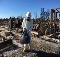 Person in hazmat suit cleaning fire damaged outdoor area